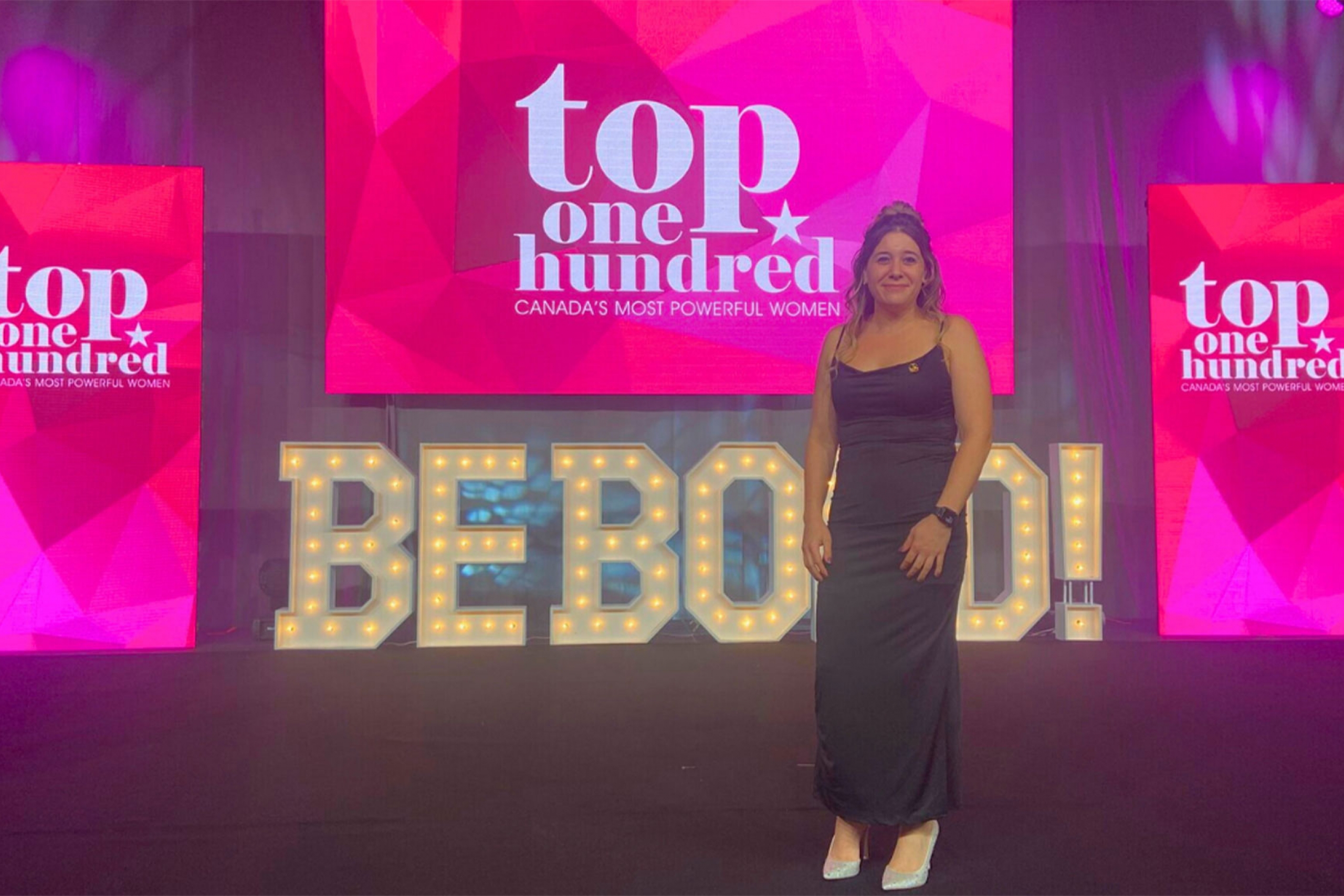 Melanie Lalonde wearing a black dress in front of the Be Bold signage.