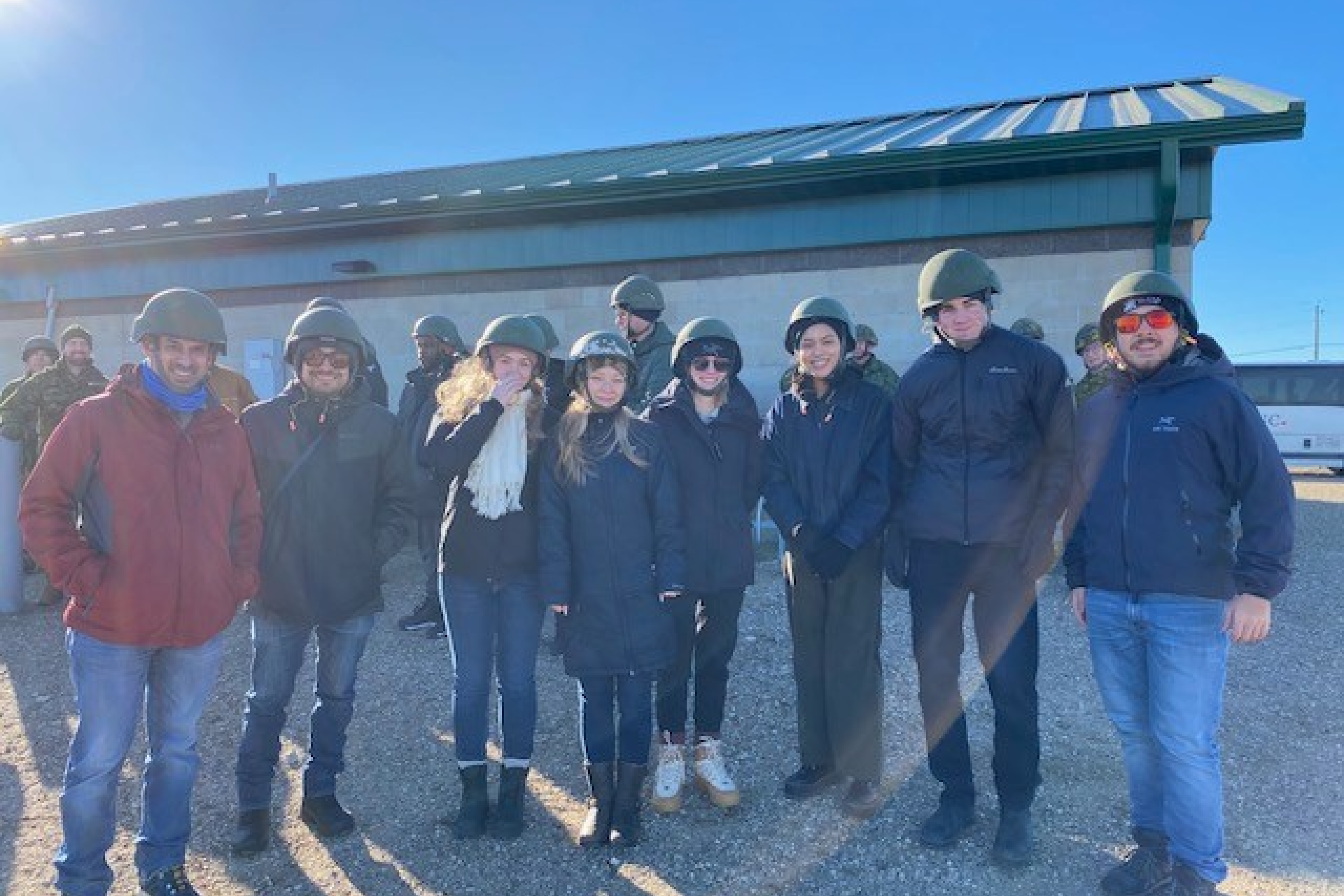 Group of eight students standing in a row, all wearing military helmets.