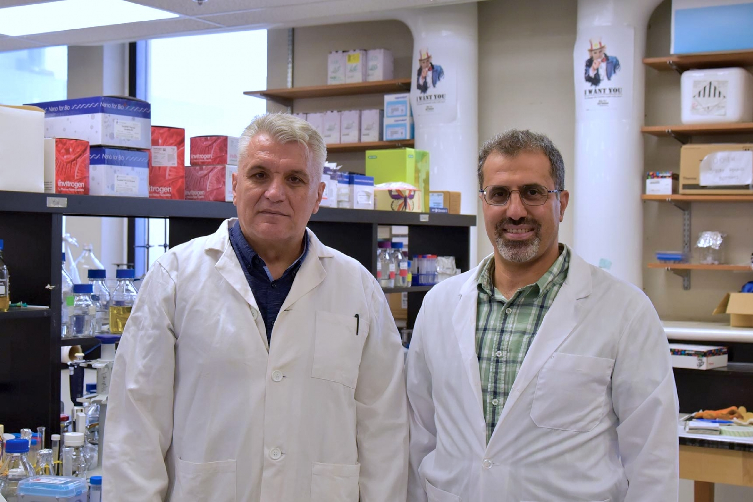 Ned and Hamid wearing lab coats and smiling at the camera.