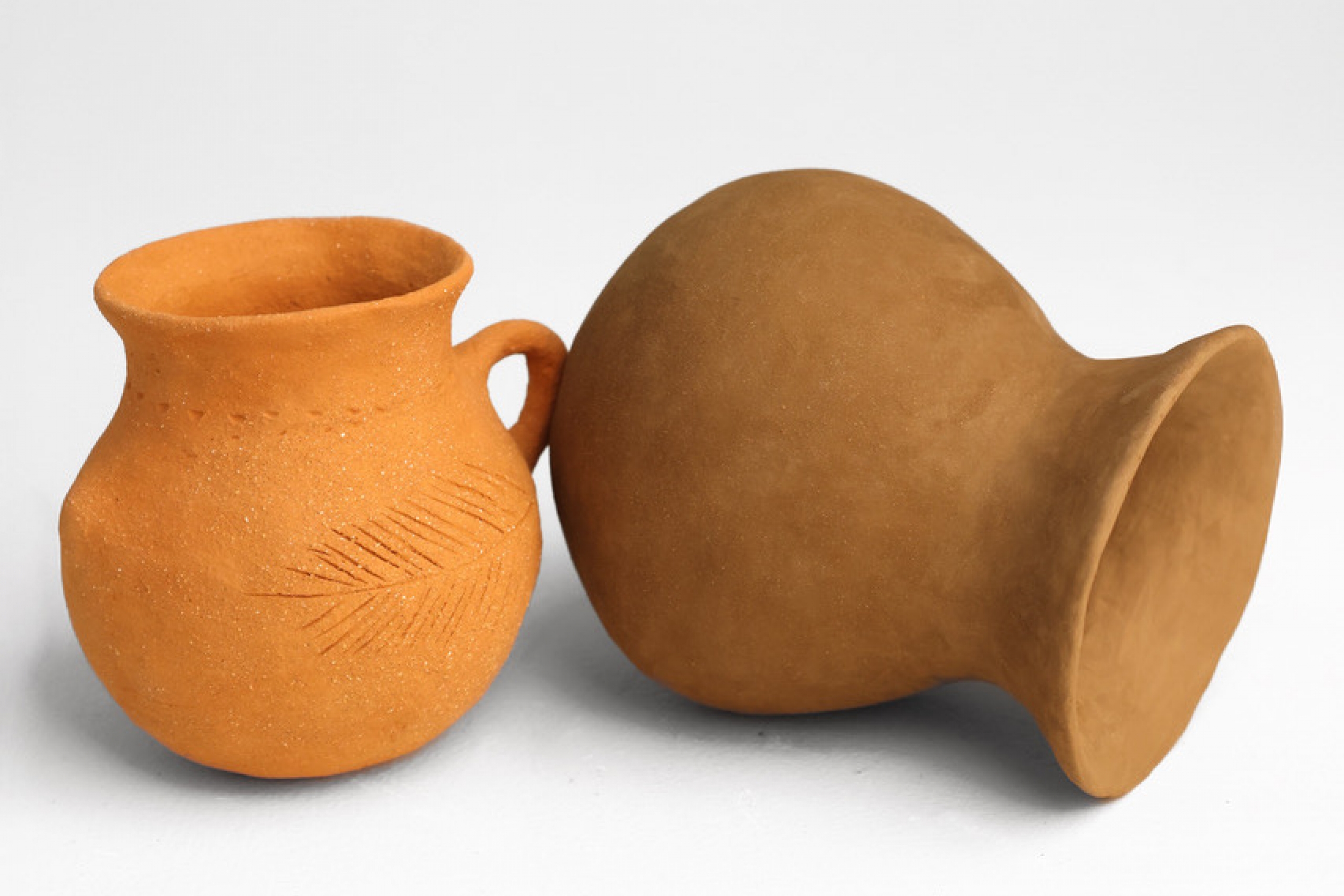 Two hand-built clay vessels made from locally sourced Manitoba clay, one upright with carved decoration and one lying on its side.