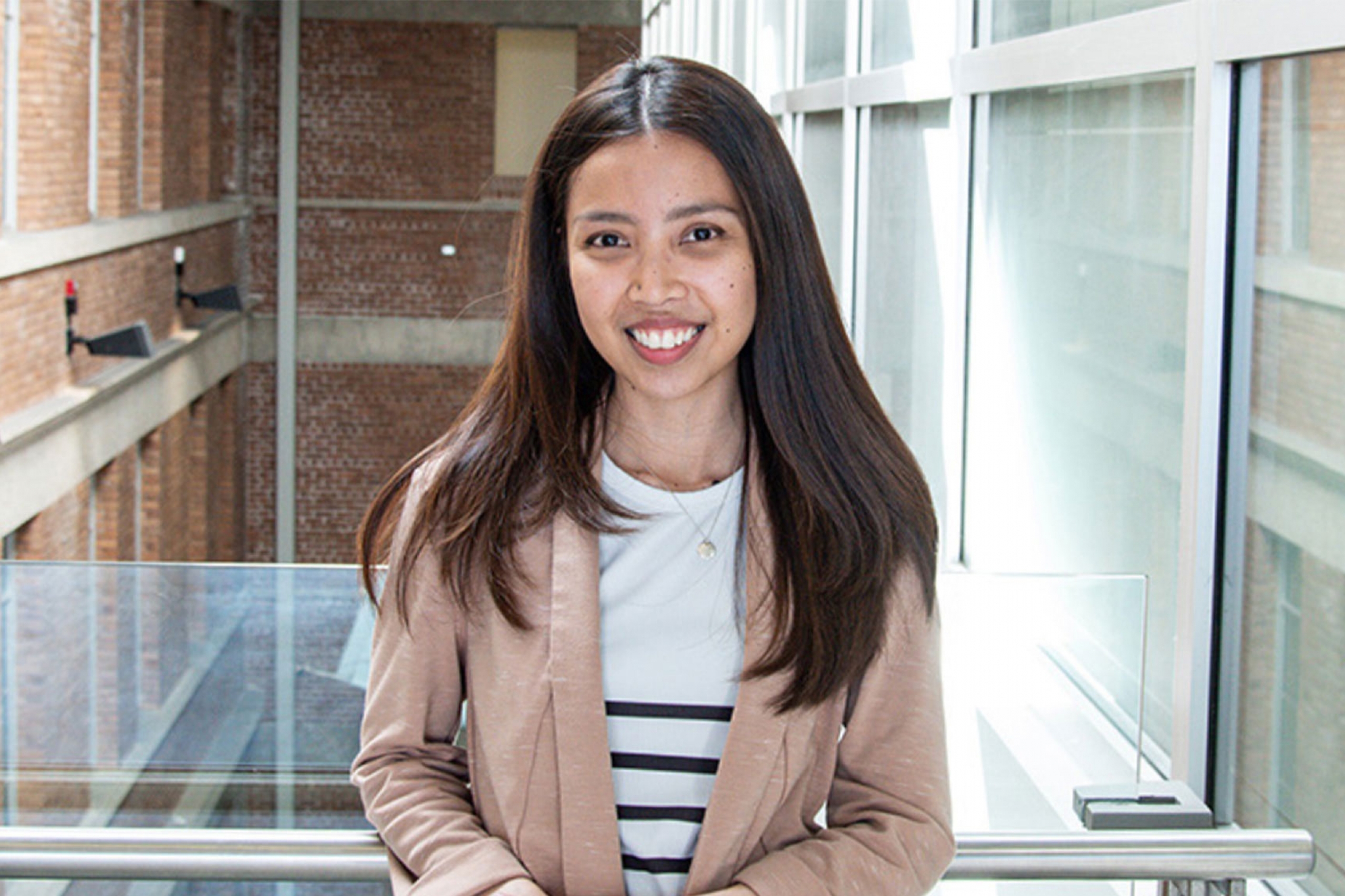Riya Timpog wearing a brown coat and smiling at the camera.