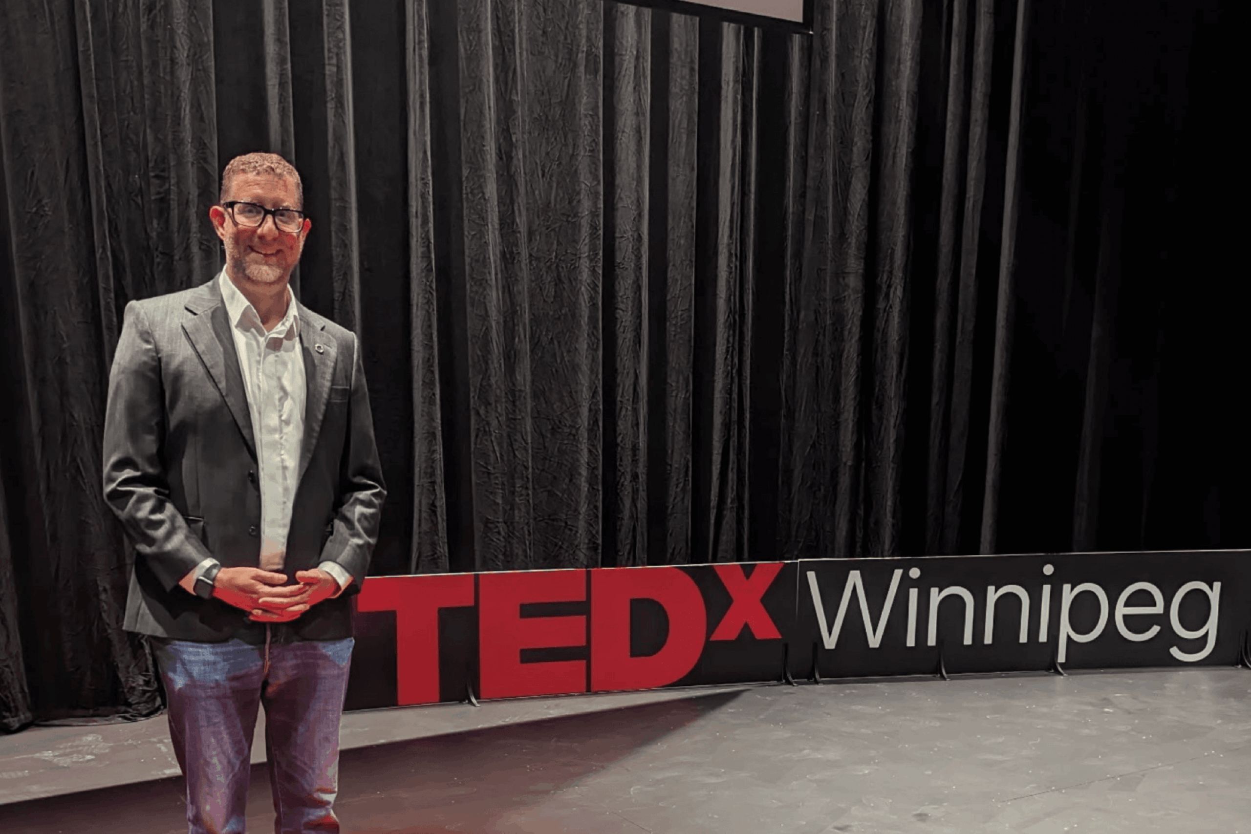 robert mizzi wearing suit and glasses standing next to tedx sign.