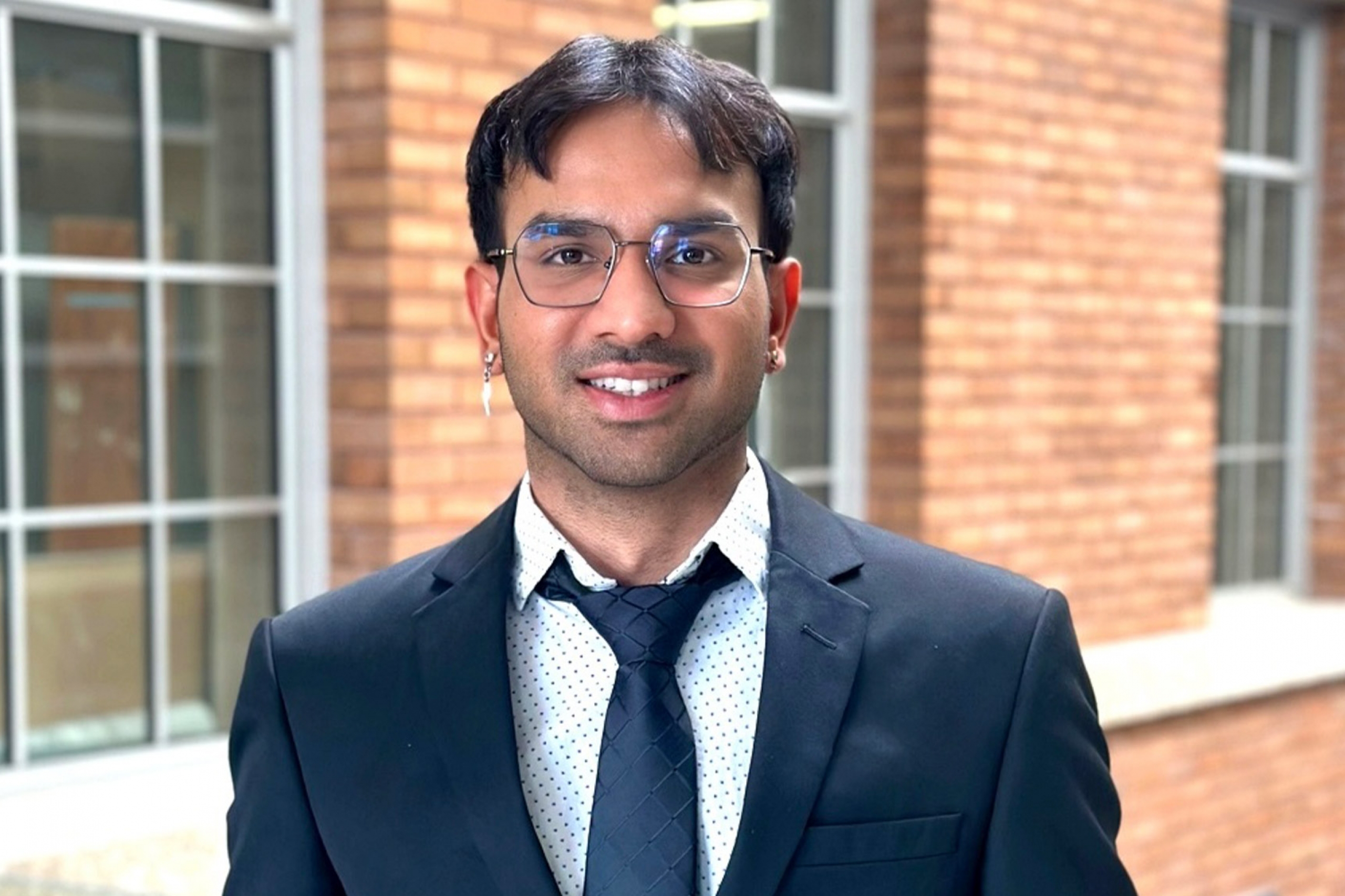 Rudra Patel wearing a blue coat and tie smiling at the camera.