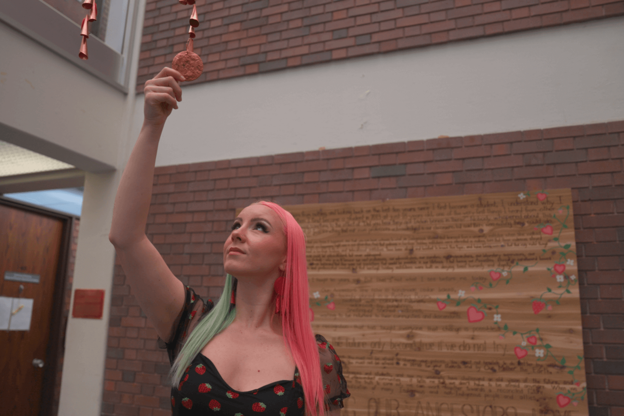 female reaches for copper jingles hanging from atrium.