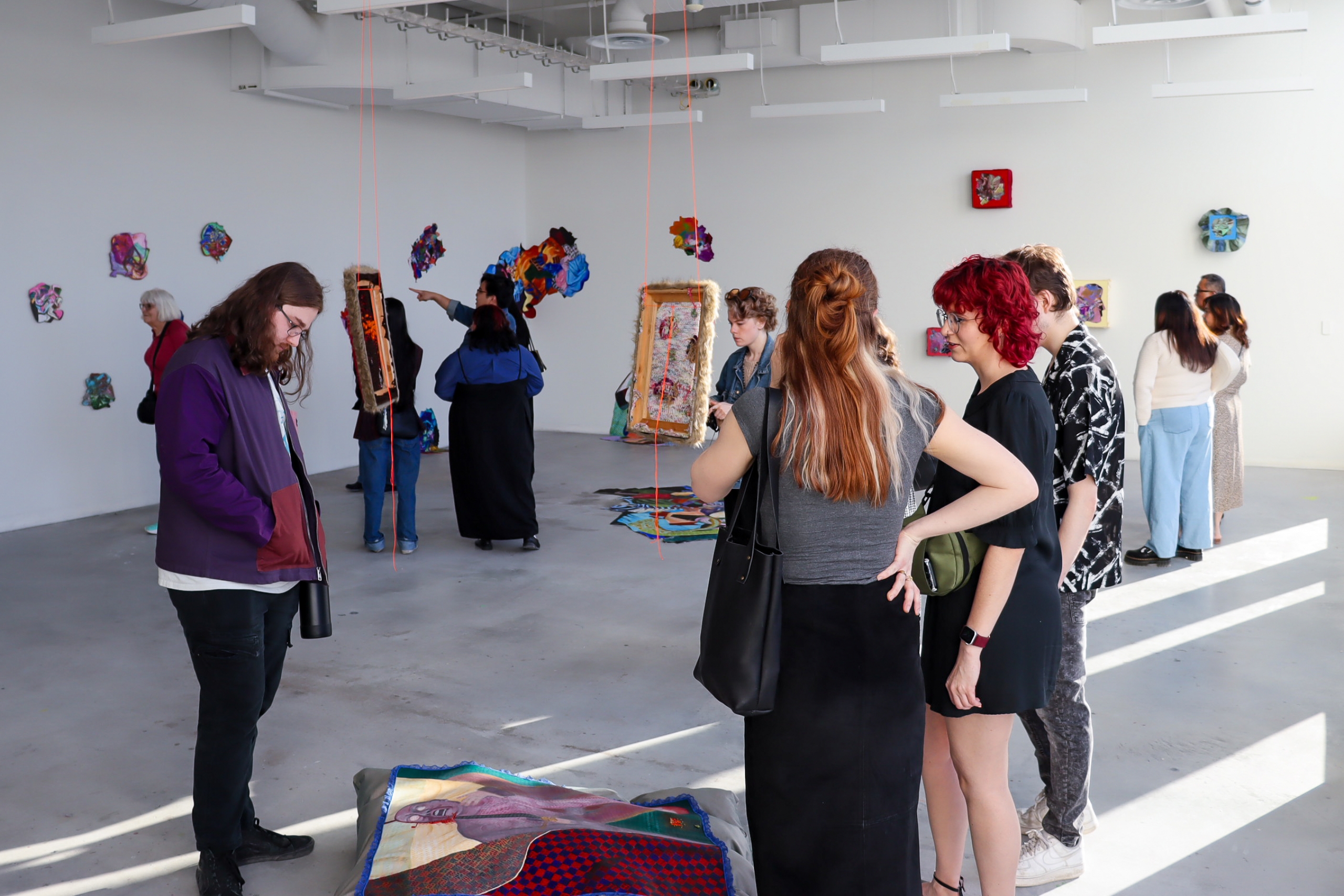 Visitors view colourful mixed-media artworks installed throughout a bright gallery space at the School of Art, University of Manitoba.