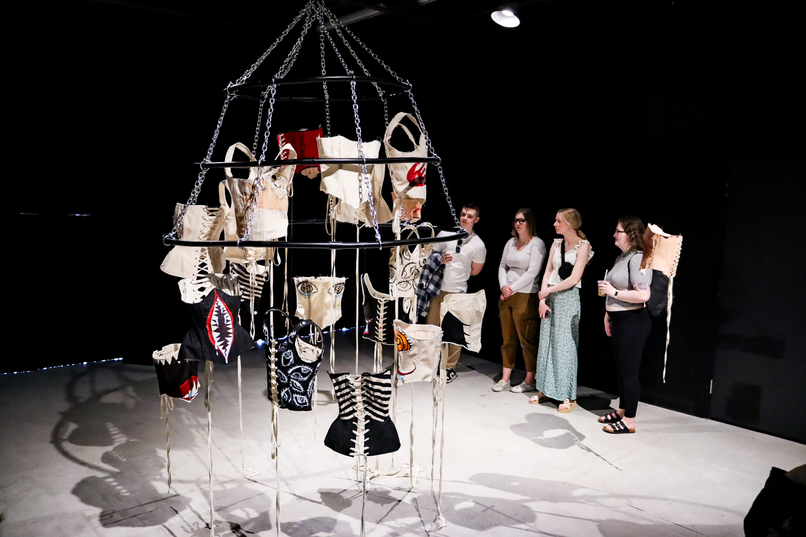 Visitors observe a suspended installation of stitched, garment-like sculptures at the School of Art, University of Manitoba.