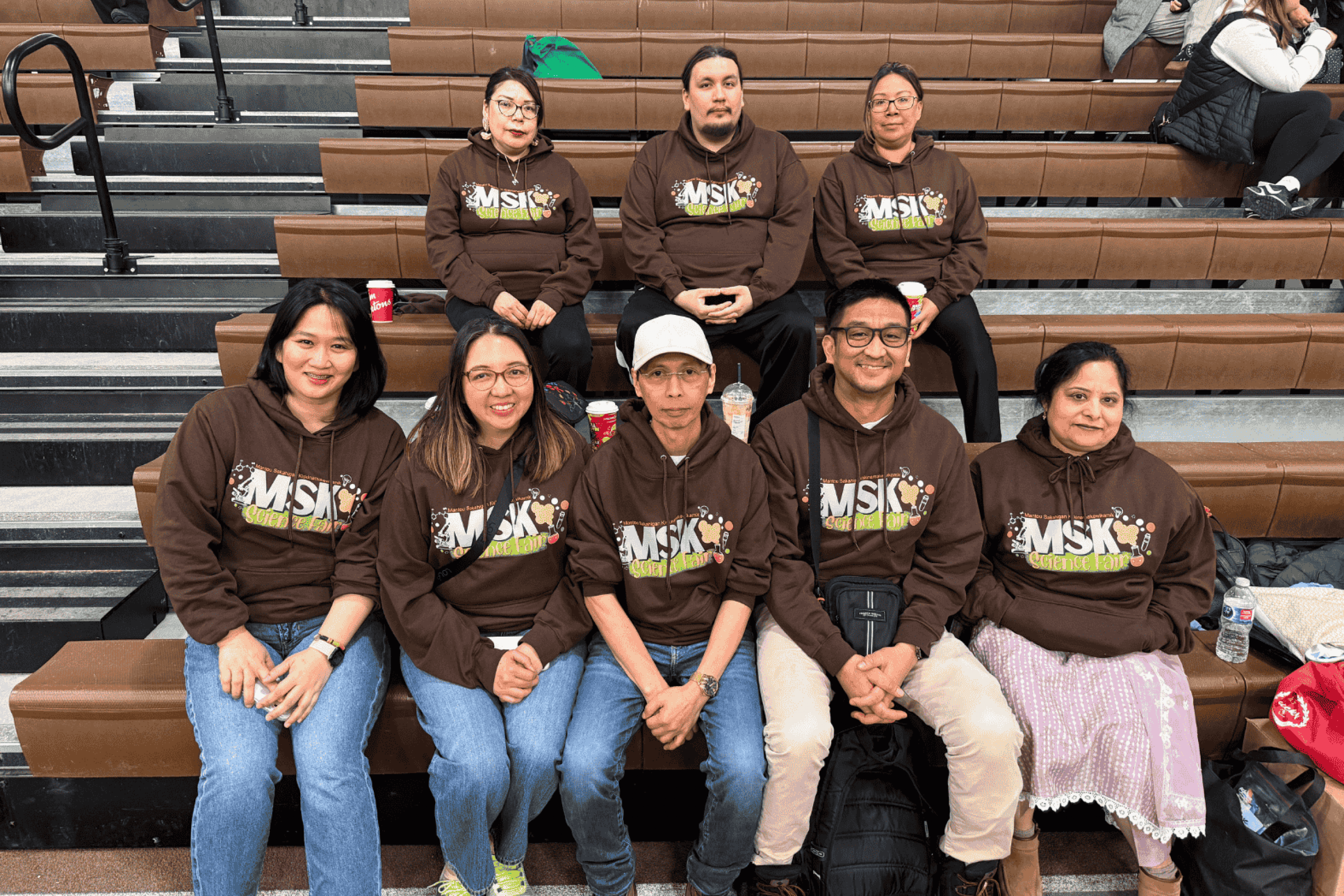 A group of people wearing matching MSK Science Fair hoodies seated together on bleachers.
