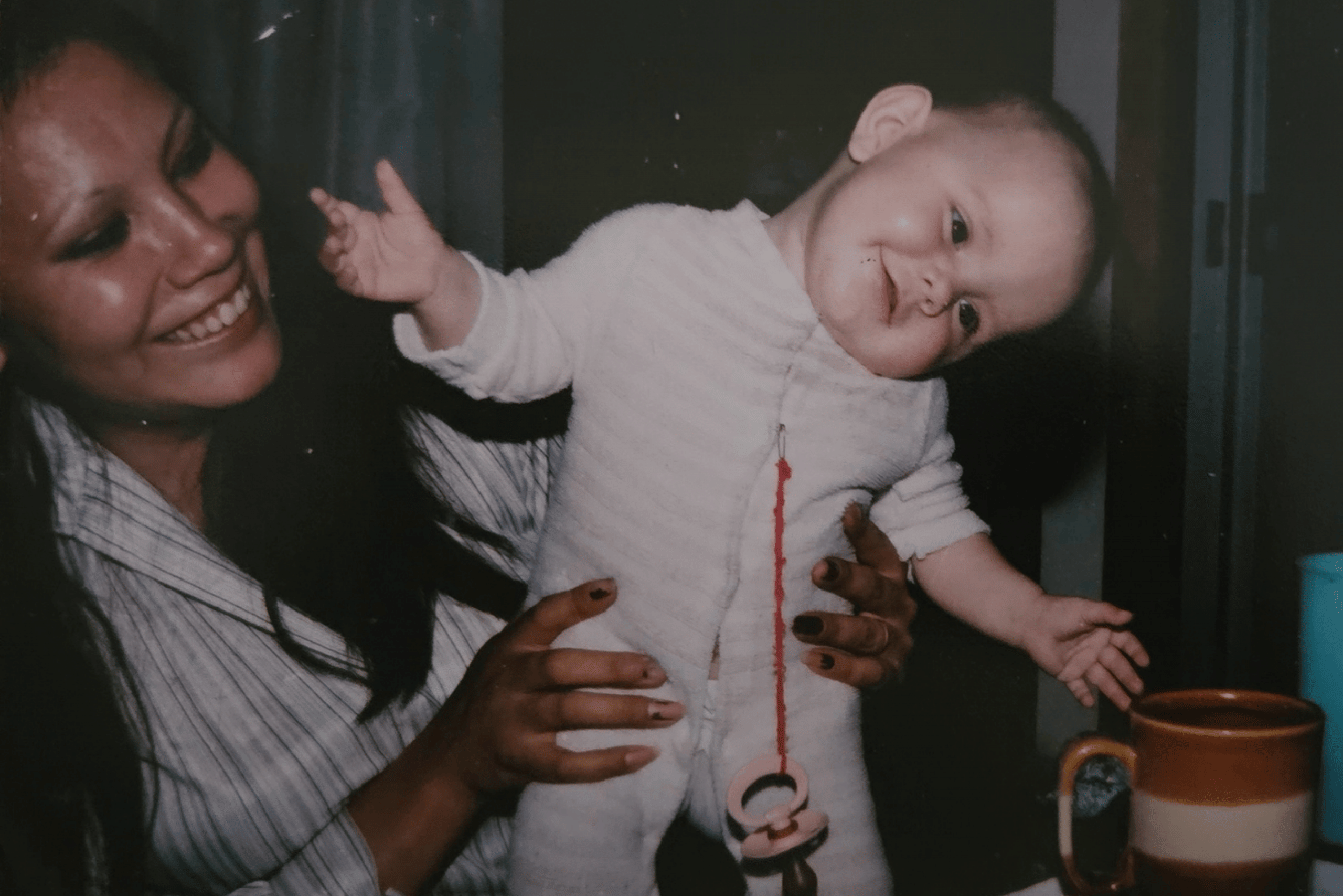 A smiling baby, held upright by her smiling mother.