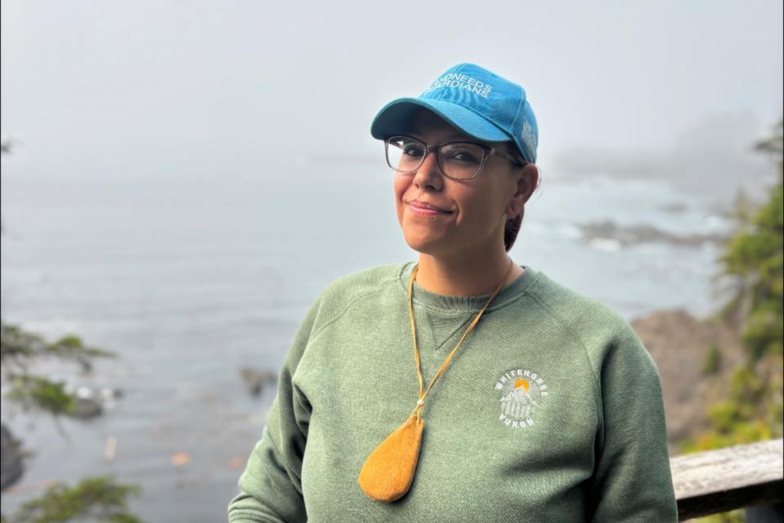 Taylor smiles while wearing her medicine pouch with water landscape in the background.