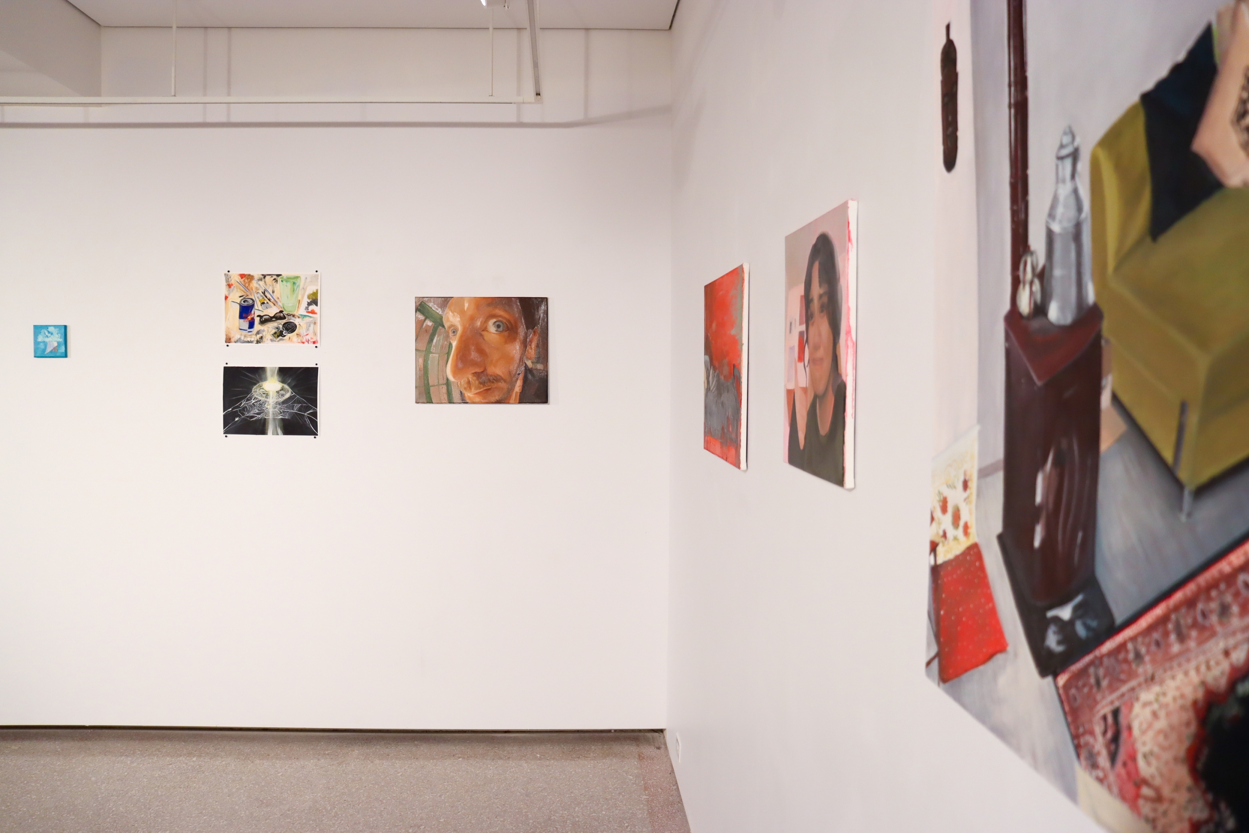 Installation view of the east gallery wall showing small works on paper alongside a large-scale figurative painting cropped at the frame's edge.