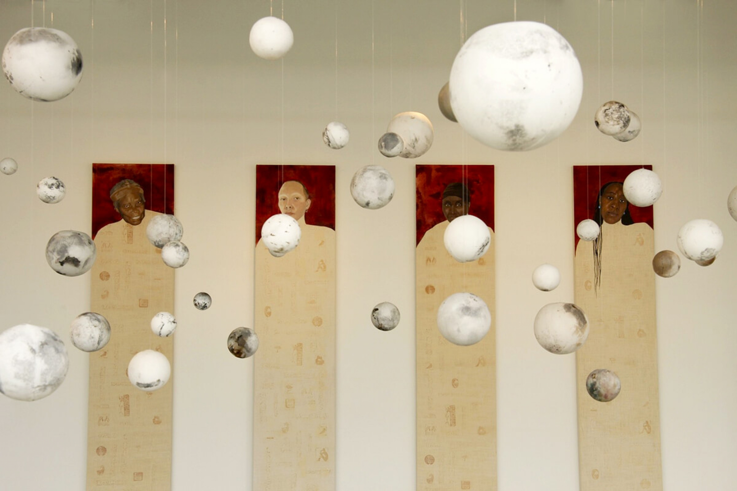 White and grey globes hand in front of four long paintings of people
