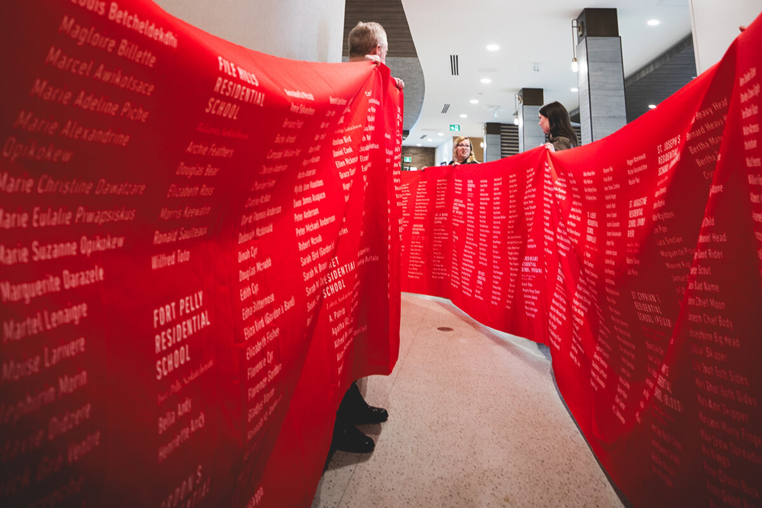 A red memorial cloth stretches out in the frame of the photo, with people stood behind, holding it up