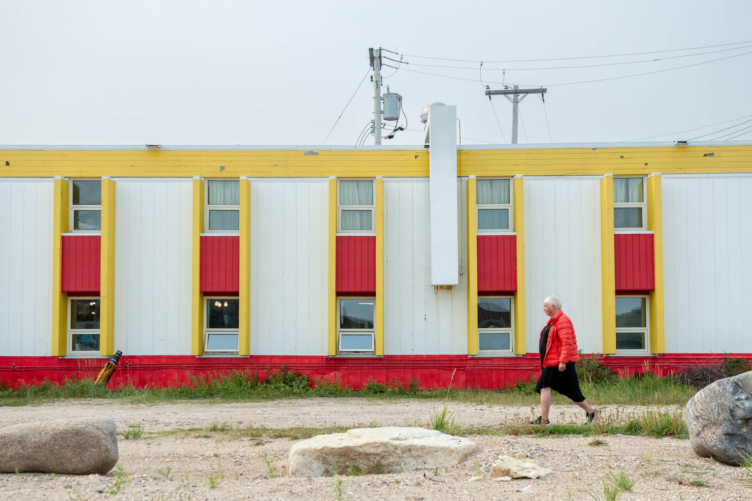 A woman in an orage coat walks past a yellow and red building