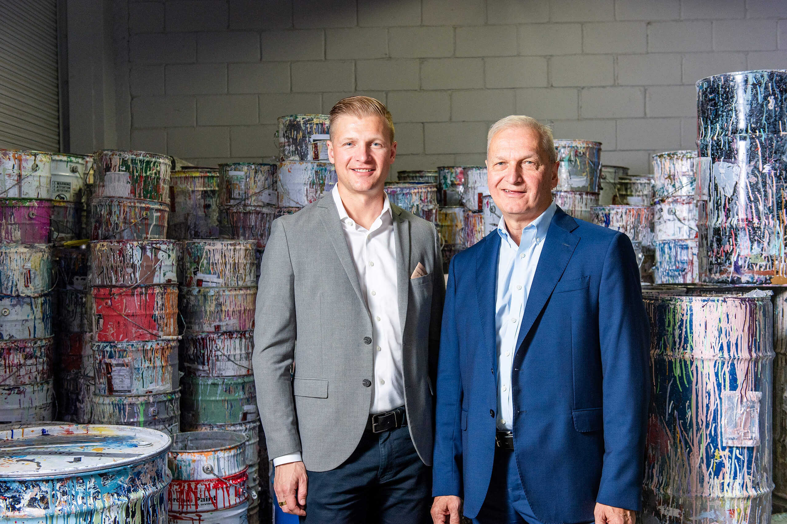 Two men standing in front of large paint cans