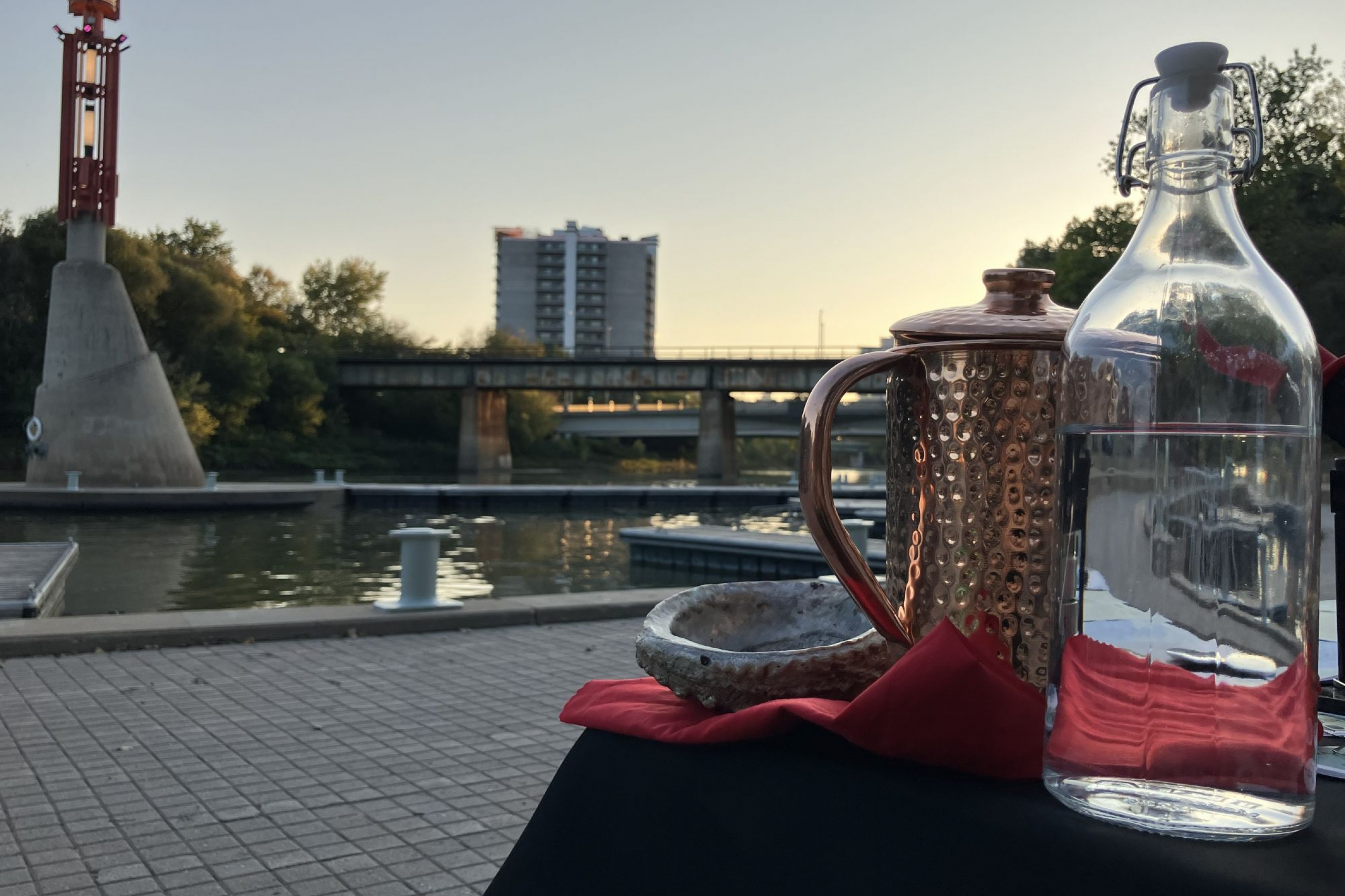 Copper water vessel, clear glass water bottle, and smudge bowl in front of the Assiniboine River