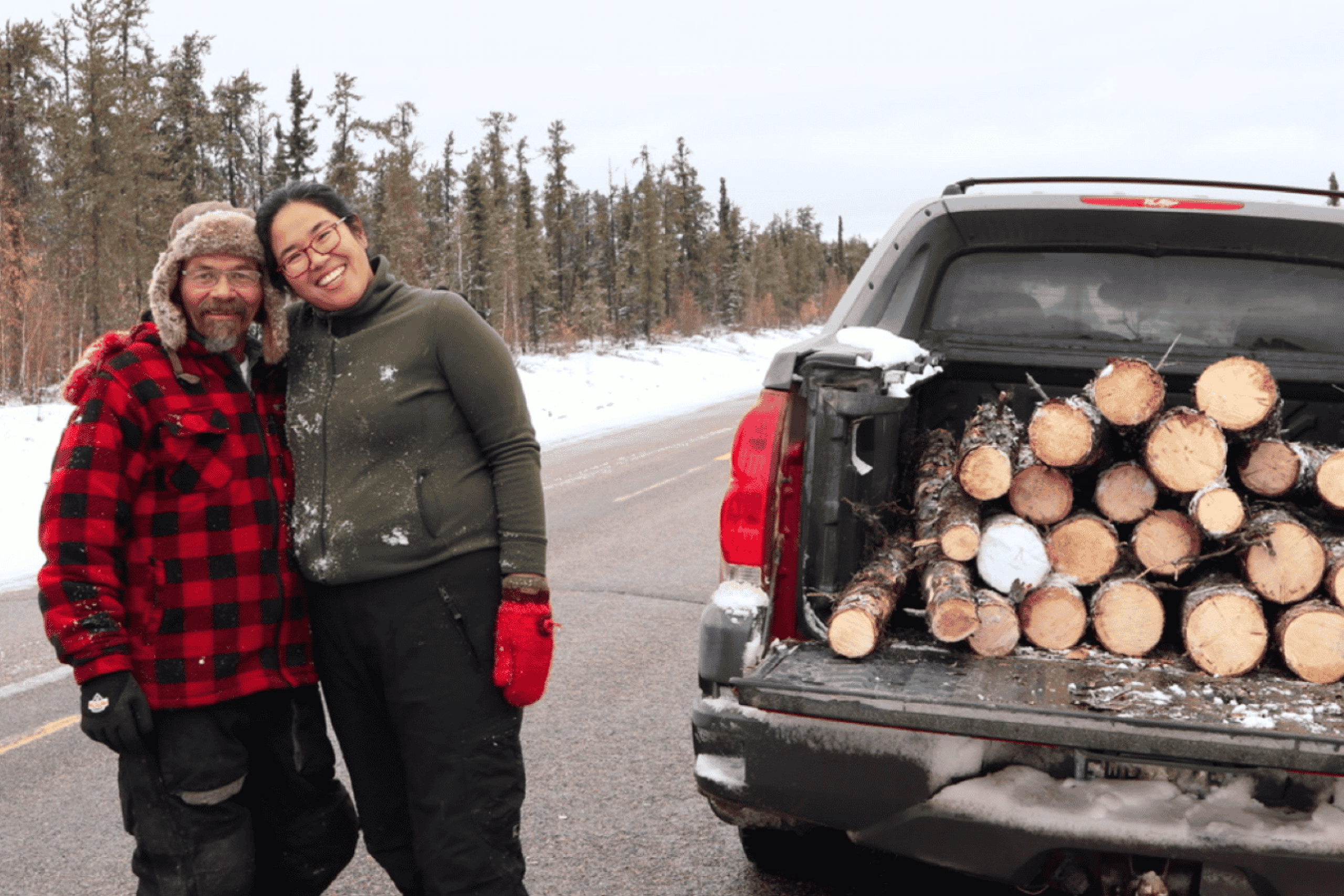 16. Two participants stand beside a truck loaded with firewood during a winter land-based activity.