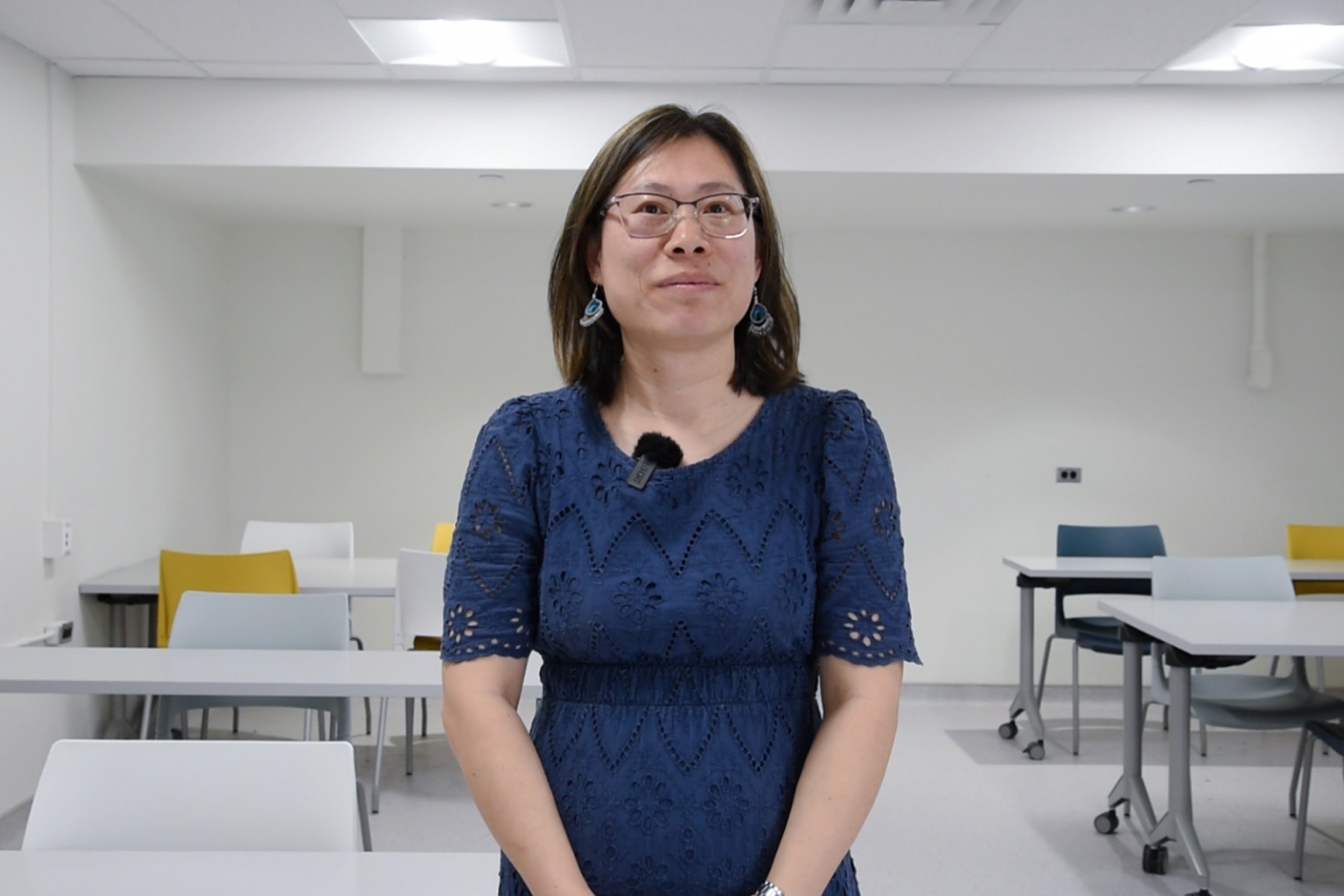 Xinli Wang wearing a blue dress and an eyeglass smiling at the camera.