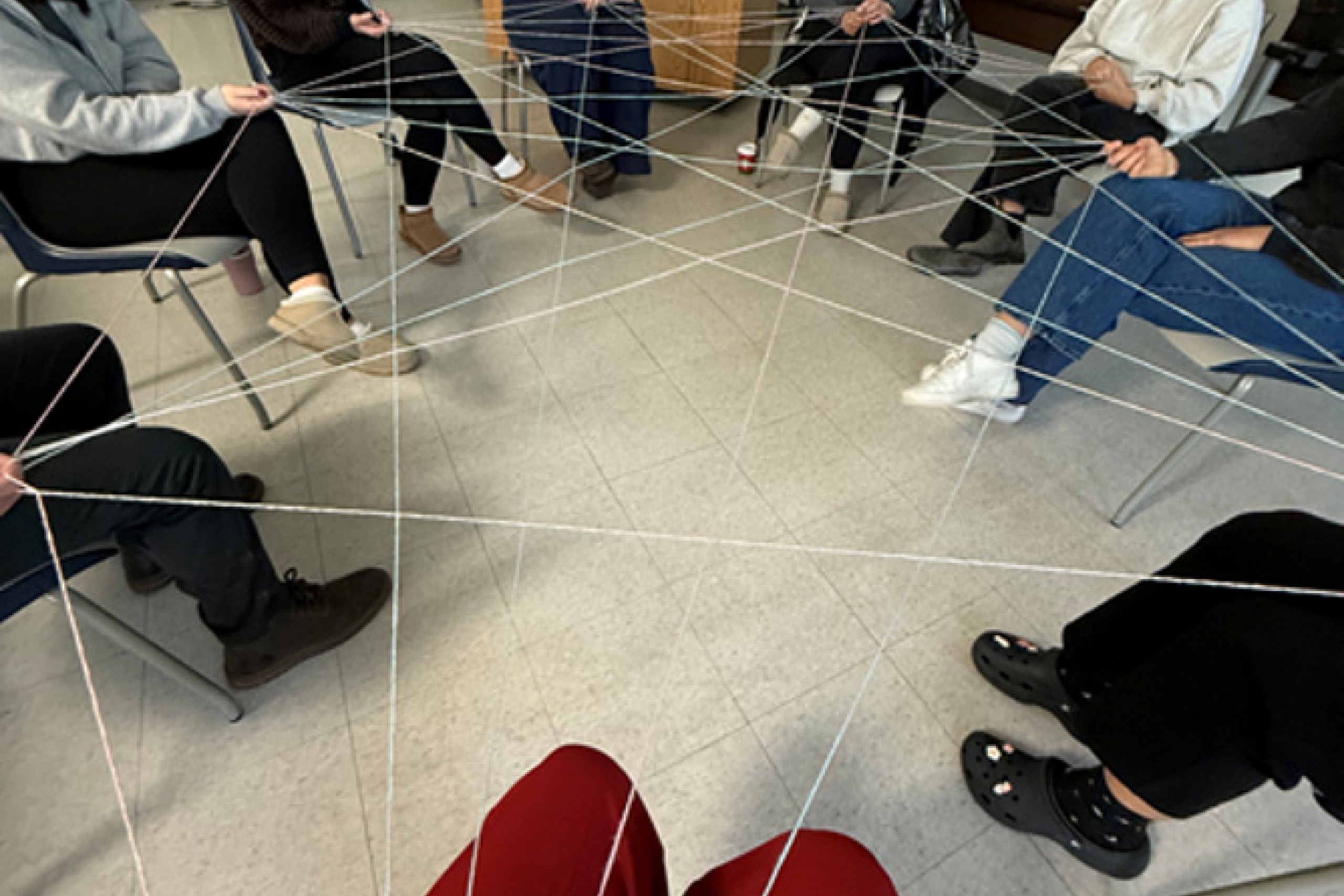 A circle of people hold an interconnected piece of yarn.