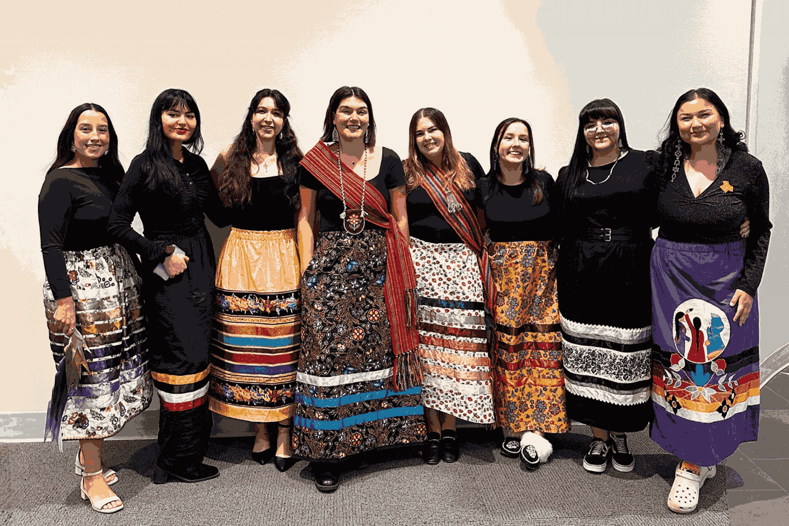 Eight students stand together wearing ribbon skirts and smiling for a group photo.